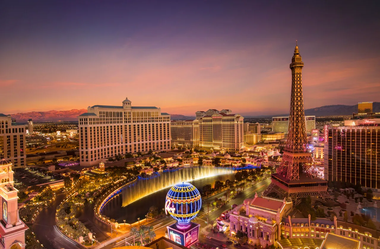 Las Vegas Strip skyline at blue hour with illuminated resort towers, a replica tower, and fountains