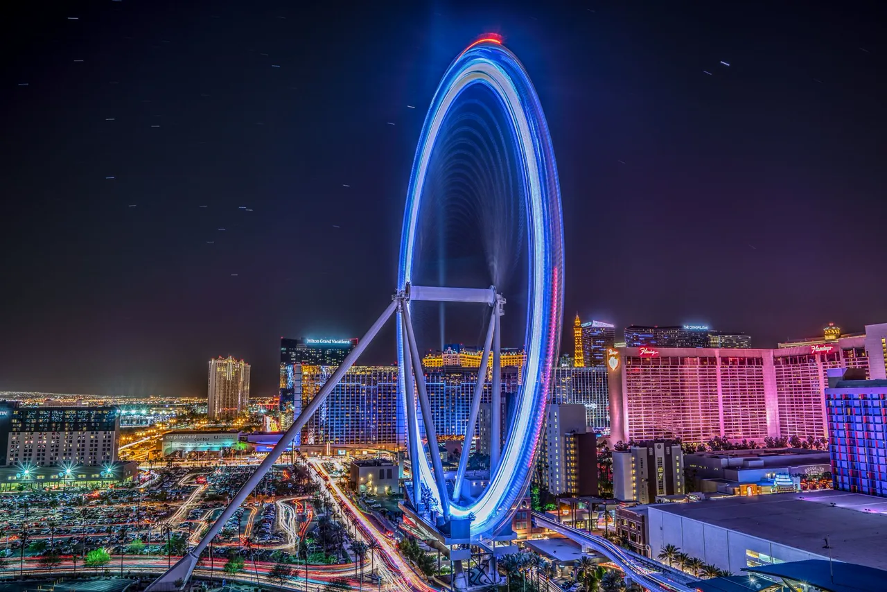 Illuminated observation wheel glowing over a nighttime city skyline of lit resort towers